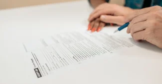 Main d'un acheteur signant des documents immobiliers à un bureau notarial avec clés et calendrier