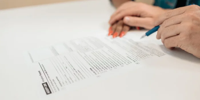 Main d'un acheteur signant des documents immobiliers à un bureau notarial avec clés et calendrier