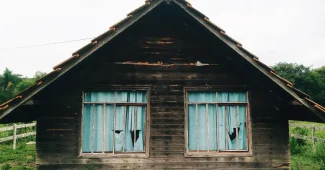 Maison abandonnée avec volets fermés et façade détériorée, envahie par la végétation