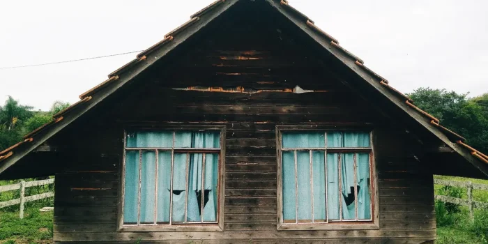 Maison abandonnée avec volets fermés et façade détériorée, envahie par la végétation