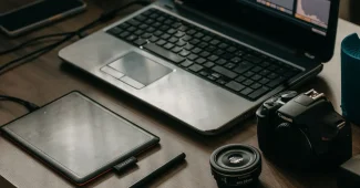 Mains d'un créateur arrangeant des produits POD sur un bureau avec ordinateur affichant une boutique en ligne