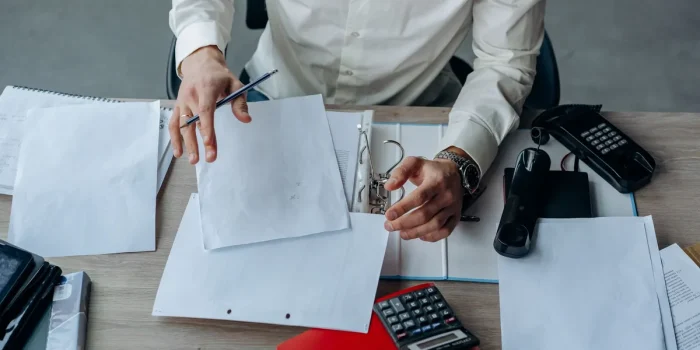 Mains tenant des documents et formulaires administratifs sur un bureau avec stylo et lunettes