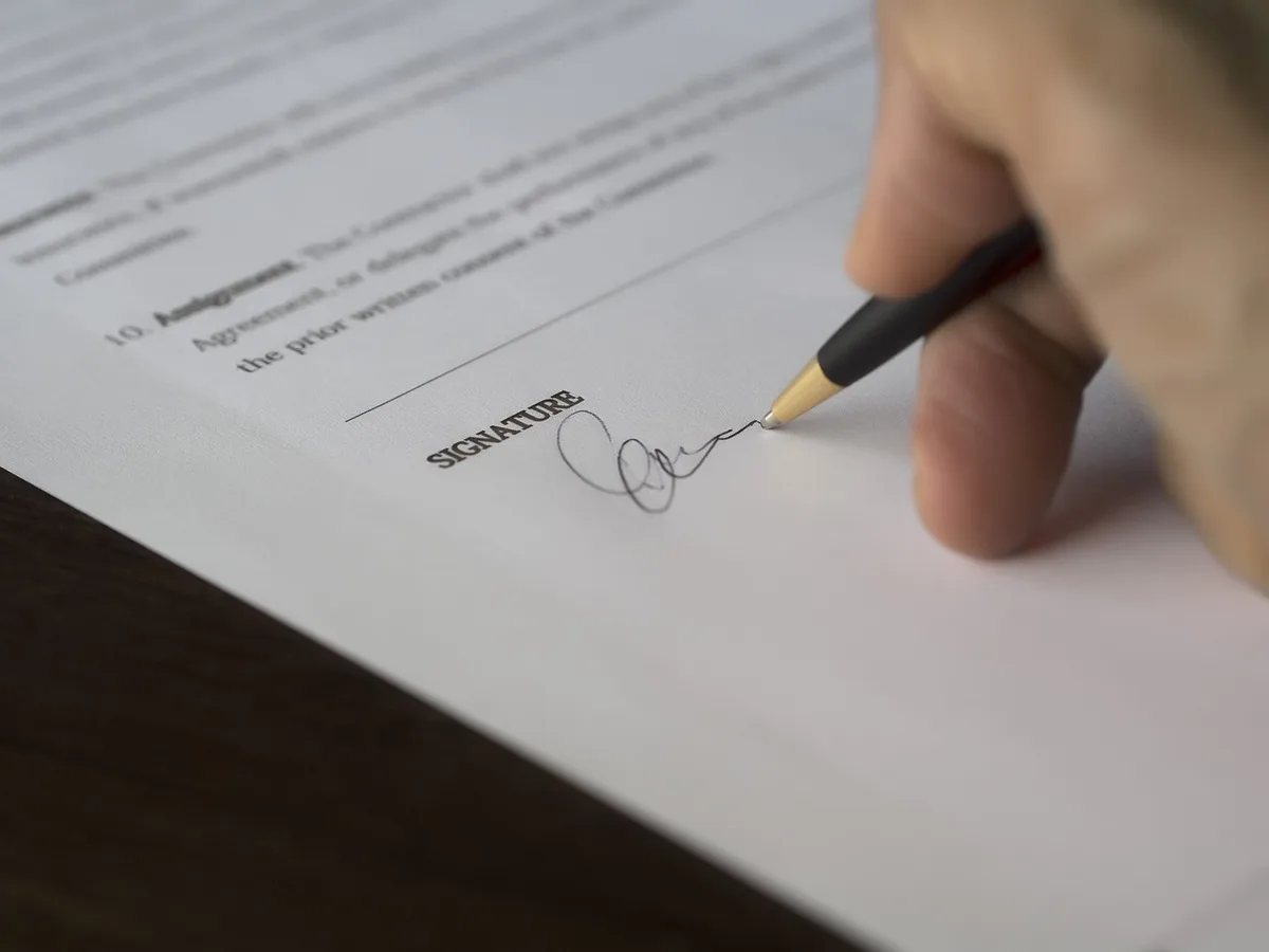 Personne signant un contrat d'assurance sur une table éclairée par la journée