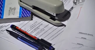Mains tenant des documents administratifs et une tablette affichant un registre commercial, sur un bureau professionnel