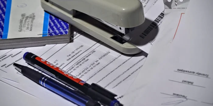 Mains tenant des documents administratifs et une tablette affichant un registre commercial, sur un bureau professionnel