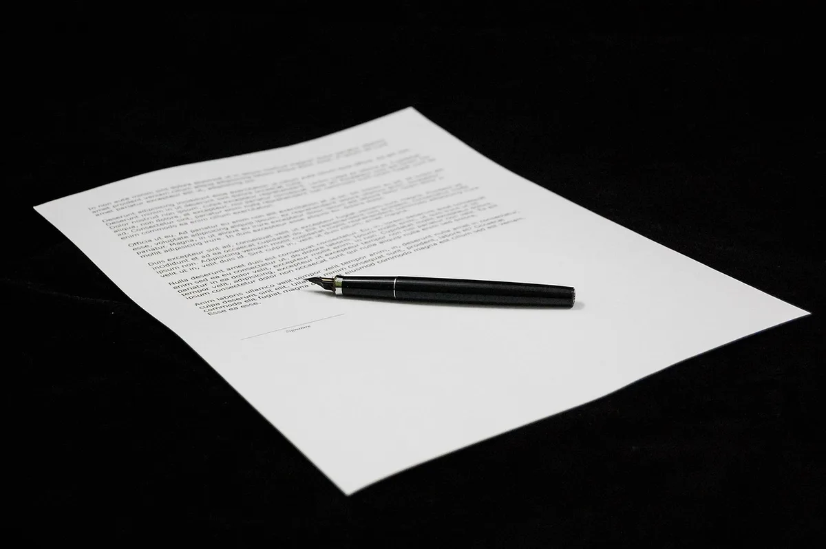 Une personne signe un contrat de sous‑location sur une table ensoleillée